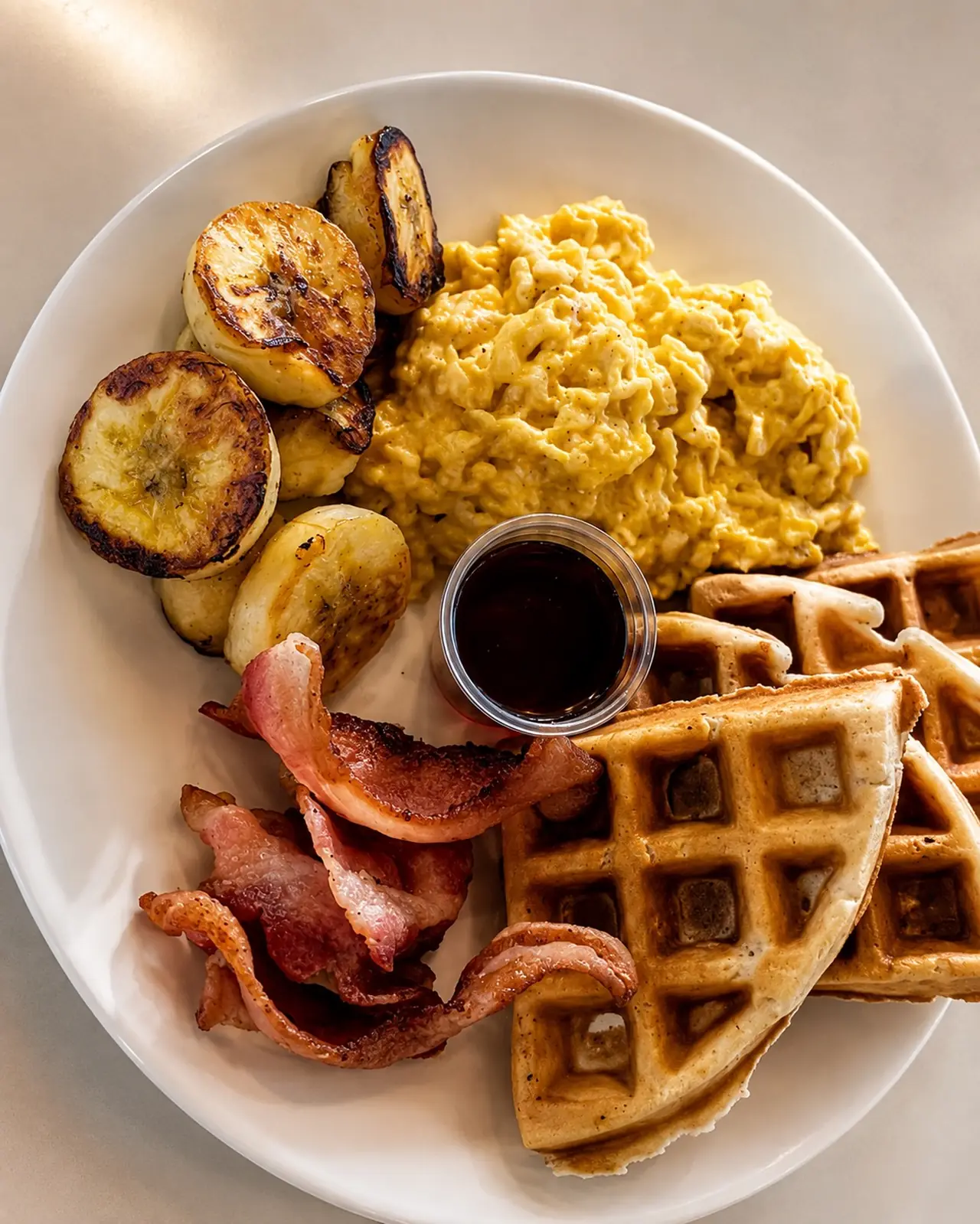 Breakfast Special plate: scrambled eggs, crispy bacon, fried plantain and waffles with syrup
