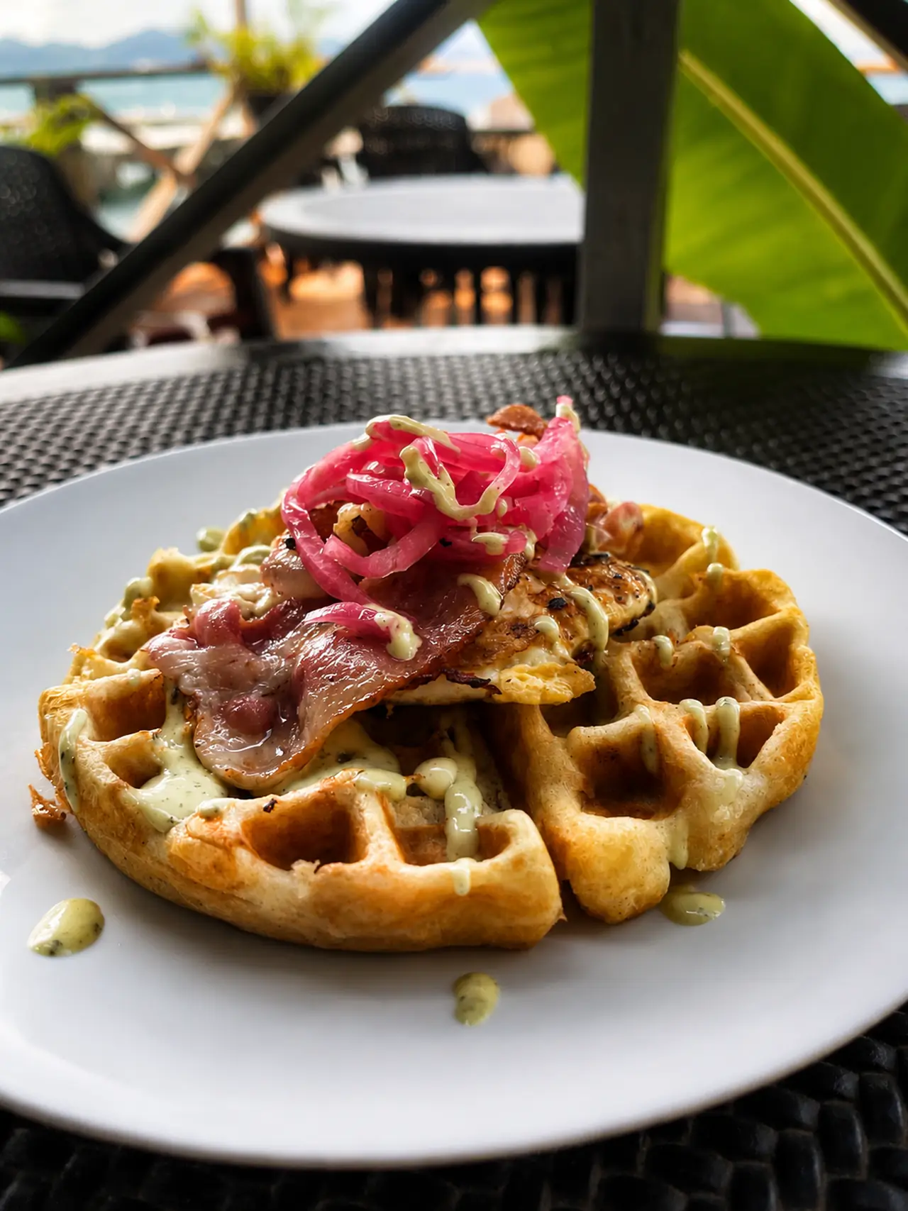 Savoury breakfast waffle topped with bacon, a fried egg and pickled red onion