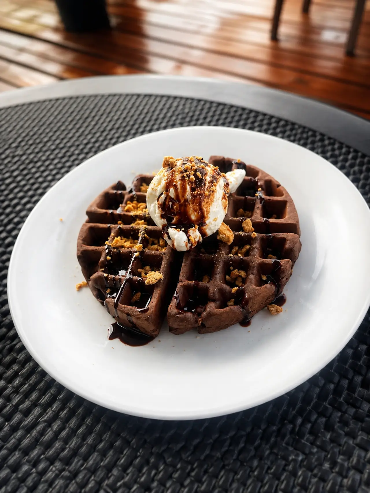 Warm chocolate waffle topped with a scoop of ice cream, chocolate sauce and nut crumble
